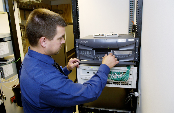 White male network technician installing a rack mounted server.